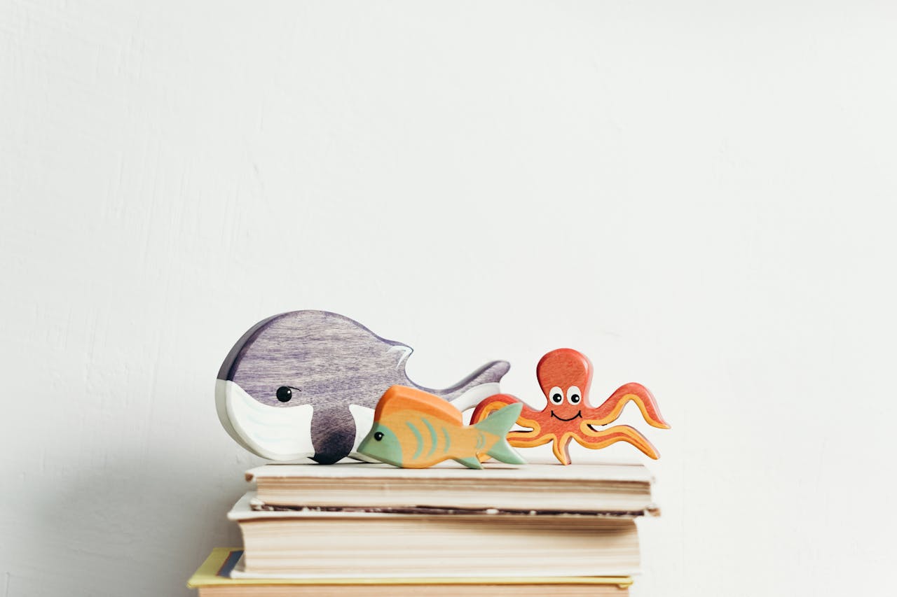 Offerings Charming wooden toys of marine animals on stacked books with a white background, perfect for kids' decor.