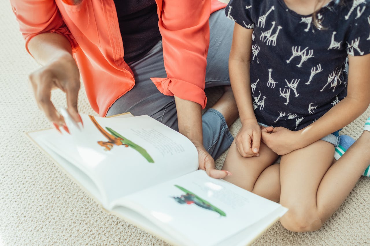 A mother and daughter sit on the floor, engaged in reading a colorful children